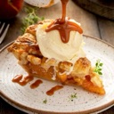 A slice of pie topped with a scoop of vanilla ice cream being drizzled with caramel sauce on a white plate.
