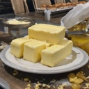 Butter sticks stacked on a white plate sitting on a wooden surface.