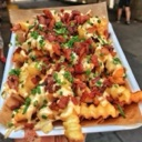 Loaded crinkle-cut fries topped with melted cheese, bacon bits, and chopped green onions on a paper-lined tray.
