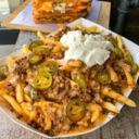 A plate of loaded fries topped with chili, melted cheese, sliced jalapeños, and a dollop of sour cream.