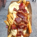 French fries topped with melted cheese and crispy bacon bits held in a paper tray.