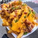 Loaded fries covered in melted cheese, bacon bits, and green onions held in a paper tray.