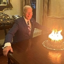 Joe Biden sits at a table staring at a birthday cake that is completely engulfed in flames.