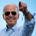 Joe Biden wearing aviator sunglasses and smiling while pointing his finger directly forward.