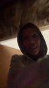 Person in a dark hoodie with a grainy, mysterious, and slightly unsettling grin.