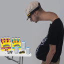A man with a distended belly leans over a table filled with various snack boxes and drinks.