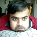A man with a tired, serious expression resting his chin on a patterned pillow.