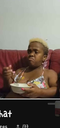 A person with a skeptical expression eating from a white bowl while sitting on a red couch.
