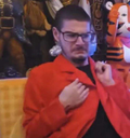 A man wearing glasses and a red jacket looking skeptical with a judgmental expression.