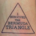 A tattoo of a triangle with the text I SURVIVED THE BERMUDA TRIANGLE written inside.