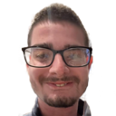 A man with a mustache and glasses smiling at the camera in a close-up selfie.