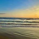 Ocean waves gently rolling onto a sandy beach during a golden sunset.