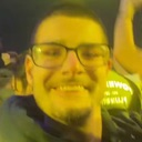 A man with glasses smiling broadly in a selfie with bright yellow lighting.