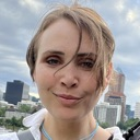 Woman with a light brown hair and a subtle, smug smirk looking directly at the camera.