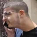 A man with short hair and glasses speaking intensely into a mobile phone.