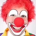 Clown with bright red hair and a red nose smiling broadly.