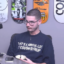 A man wearing glasses and a dark shirt stares blankly with a serious expression.
