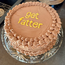 A round chocolate cake with yellow text on top that reads get fatter.