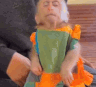 A small monkey wearing a colorful shirt looks around with a bored and unimpressed expression.