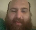A man with a beard and balding head stares blankly at the camera with a tired expression.