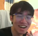 A person with dark hair and glasses laughing with a wide, genuine smile.
