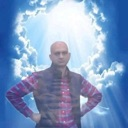 A bald man with hands on his hips stands confidently in front of a bright, cloudy sky.