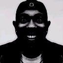 Man with a wide, intense, and unsettling grin in high-contrast black and white.