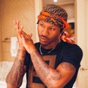 Man wearing a bandana rubbing his hands together with a smug, confident expression.