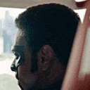 A man wearing a black mask slowly turns his head to look directly at the viewer with an intense expression.
