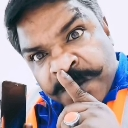A man with a thick mustache holds his index finger to his lips in a shushing gesture.