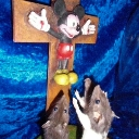 Mickey Mouse figure mounted on a wooden cross with two rats looking up at him in worship.