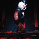 Masked warrior standing in a dark environment with red accents and a mysterious aura.
