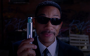 Will Smith wearing black sunglasses holds up a silver neuralyzer device.