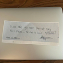A handwritten note on a laptop surface with illegible scrawled text and a signature.