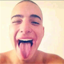 A person with a shaved head sticking their tongue out in a silly, playful expression.