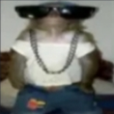 A monkey wearing dark sunglasses and a silver chain necklace looking directly at the camera.
