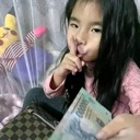 A young girl holding a stack of cash makes a shushing gesture with her finger to her lips.