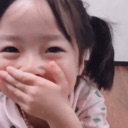 A young child laughing with their hand covering their mouth.