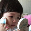 A toddler looking into a small mirror while applying makeup with a powder puff.