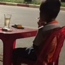 A child sits at a red table smoking a cigarette next to a glass of liquid.