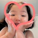 A young child smiling with their hands forming a heart shape around their face.