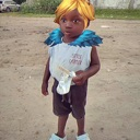 Toddler wearing a bright yellow wig and blue ruffled collar looking directly at the camera with a serious expression.