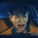 A person sitting in a car with their eyes tightly closed and mouth wide open in a dramatic crying expression.