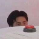 Shane Hollander peeking over a table edge at a red button with a suspicious expression.