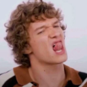 A person with curly hair making a cheeky expression with their tongue sticking out.