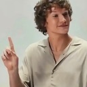 Young man with curly hair pointing his index finger up in a smug, condescending gesture.