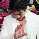 A man in a white suit holds up his hand to signal someone to wait.