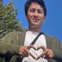 A person smiling while forming a heart shape with their hands against a clear blue sky.