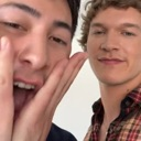Two men reacting with one person holding their face in amazement and the other smiling calmly.
