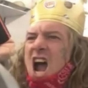 A man wearing a Burger King paper crown and a red bandana is shouting with his mouth wide open.